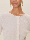 Close-up of a person wearing a textured beige cardigan with gold earrings against a neutral background