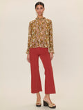 Woman wearing a patterned blouse and red pants on a beige background