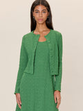 Woman wearing a green textured dress with matching cardigan on a beige background