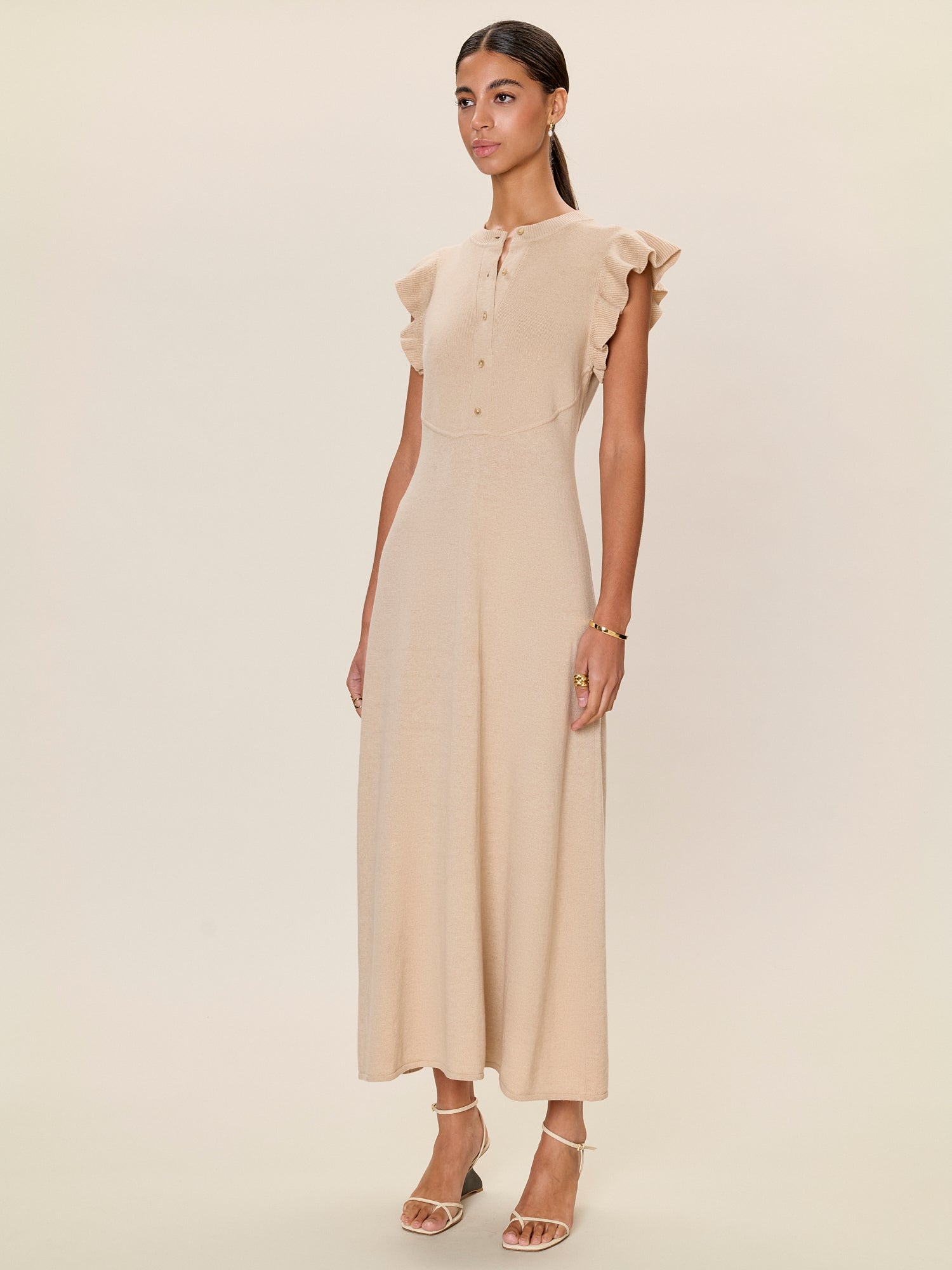 Woman wearing a beige dress with ruffled sleeves on a plain background