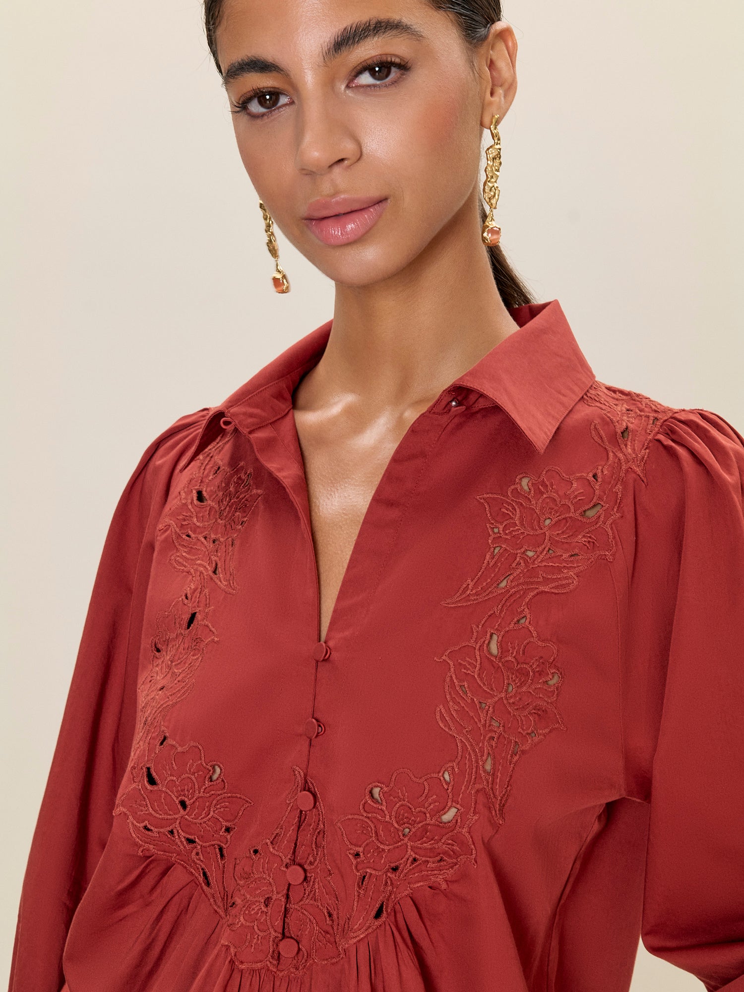 Woman wearing a red blouse with intricate lace detailing on a beige background