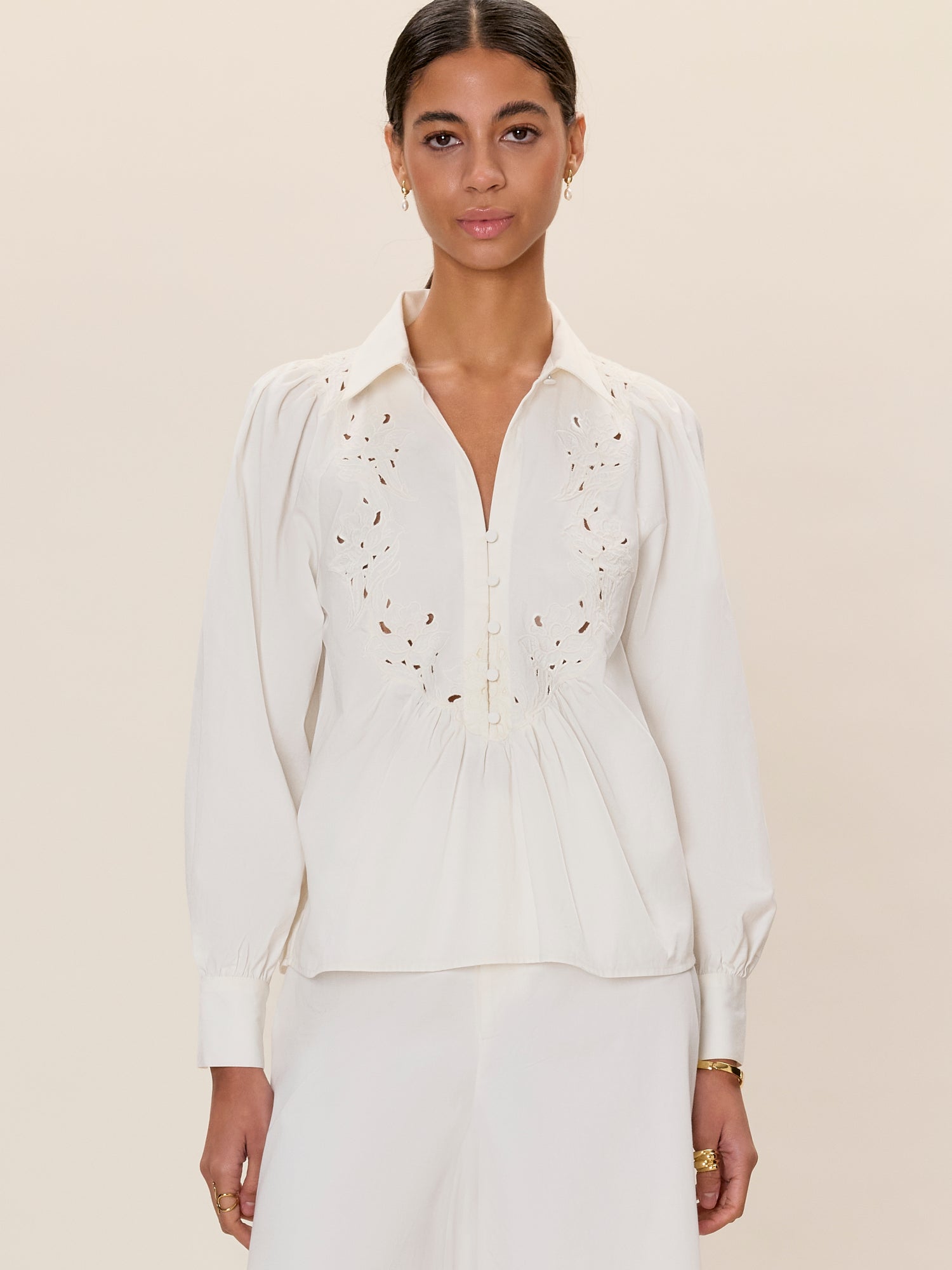Woman wearing a white blouse with intricate detailing on a beige background