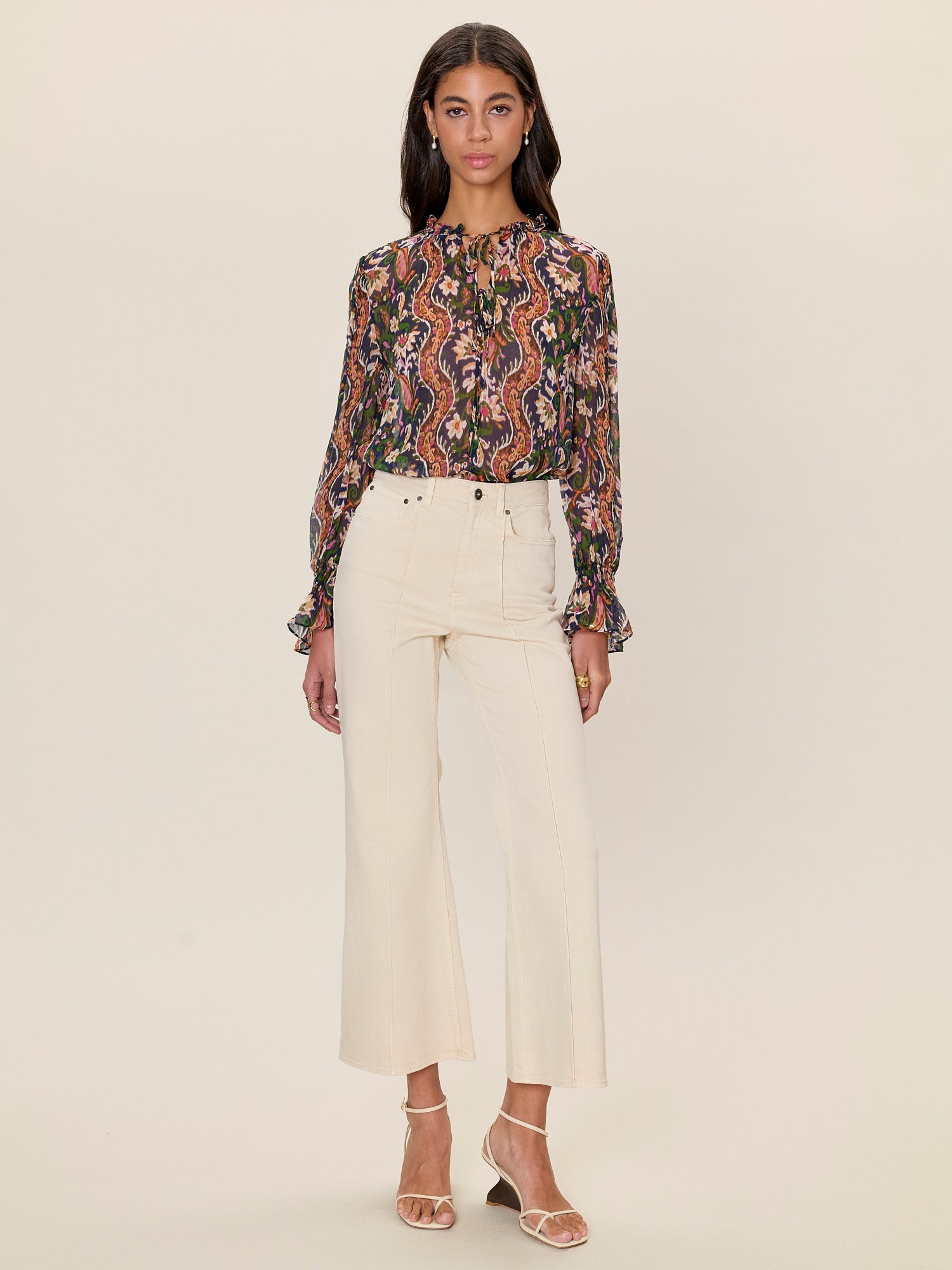 Woman wearing a patterned blouse and white pants on a beige background