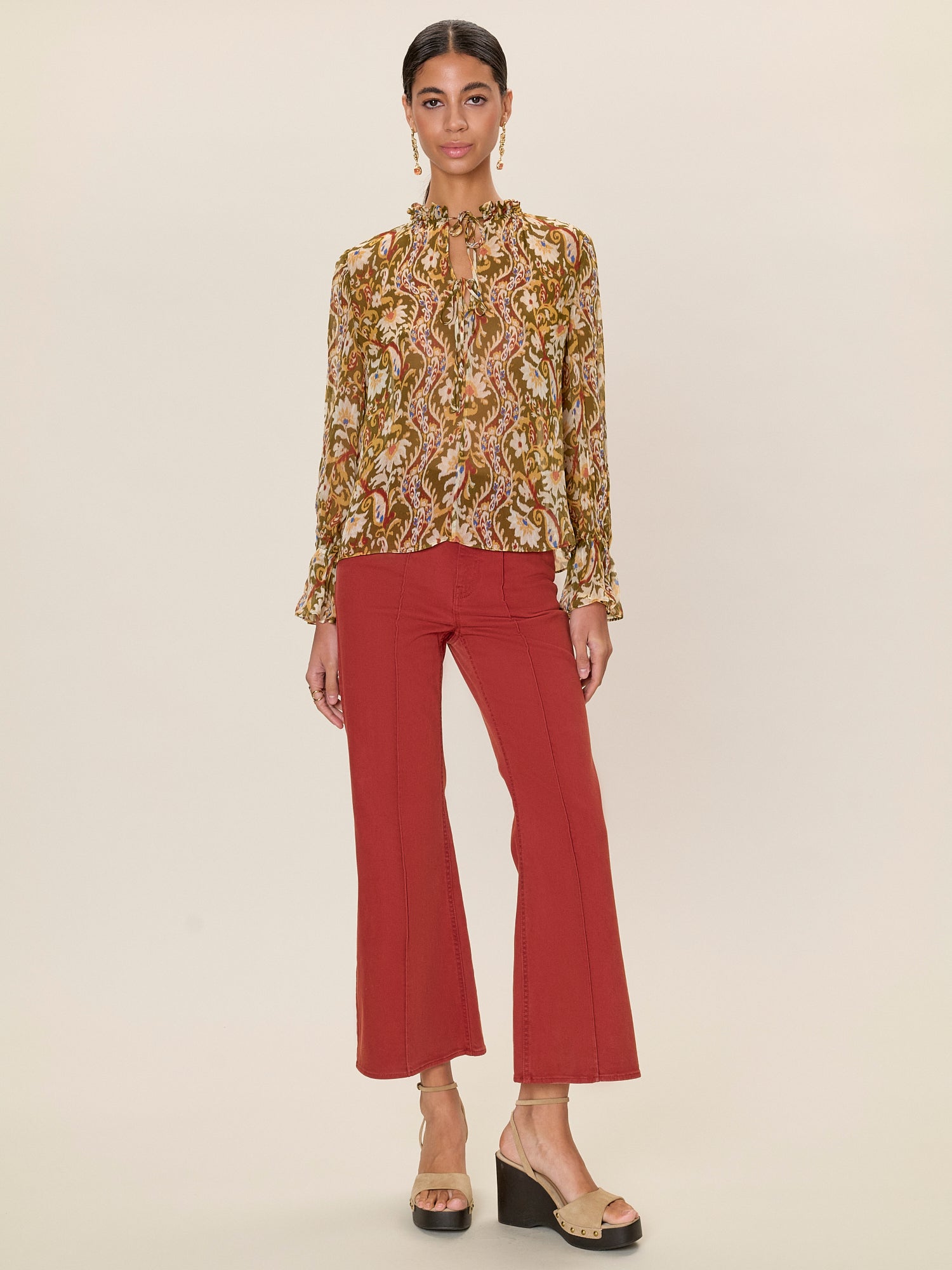 Woman wearing a patterned blouse and red pants on a beige background