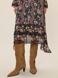 Person wearing a patterned dress with long sleeves and a high-low hemline, paired with brown knee-high boots on a beige background.