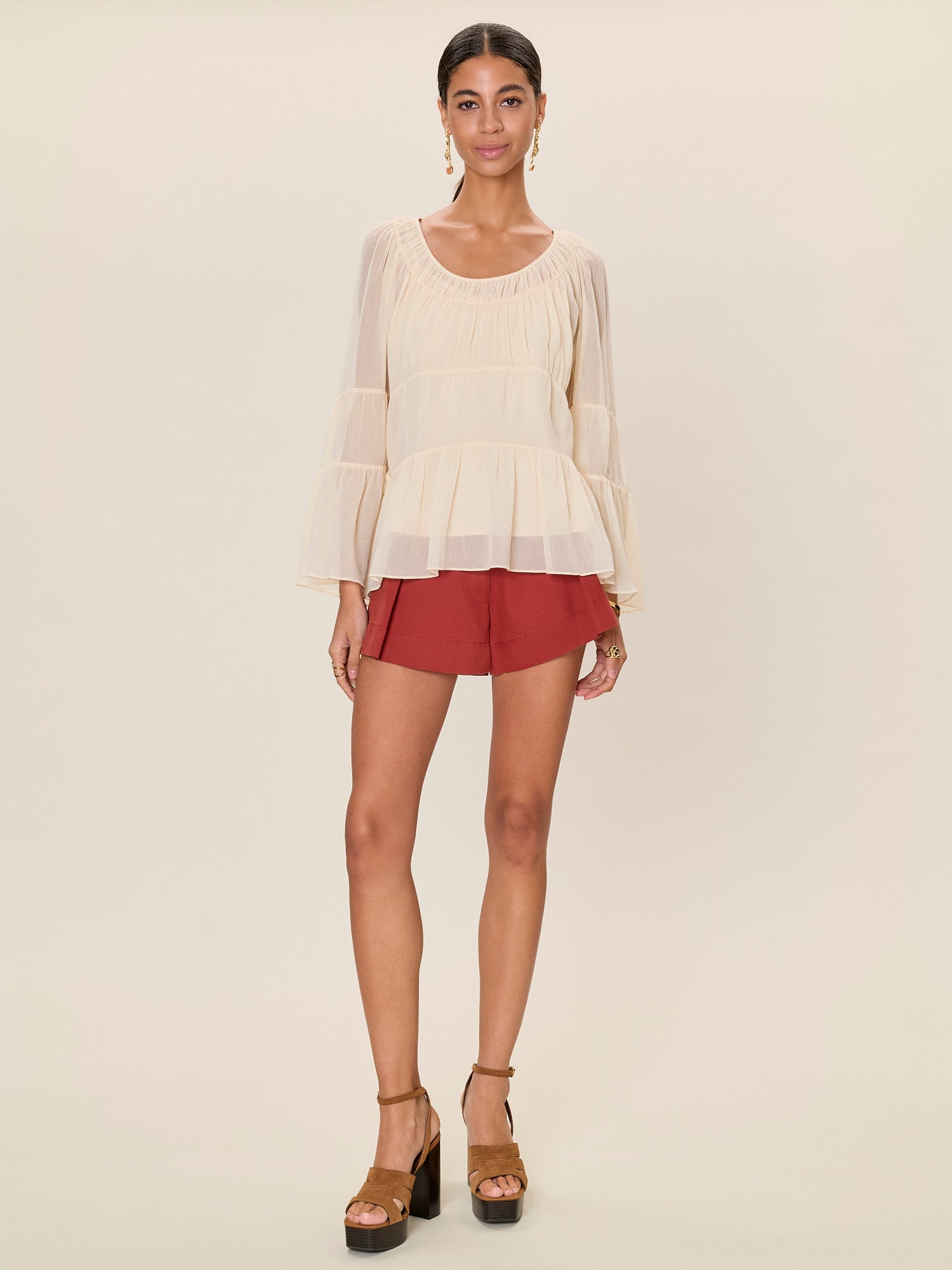 Woman wearing a beige top and red shorts on a plain background