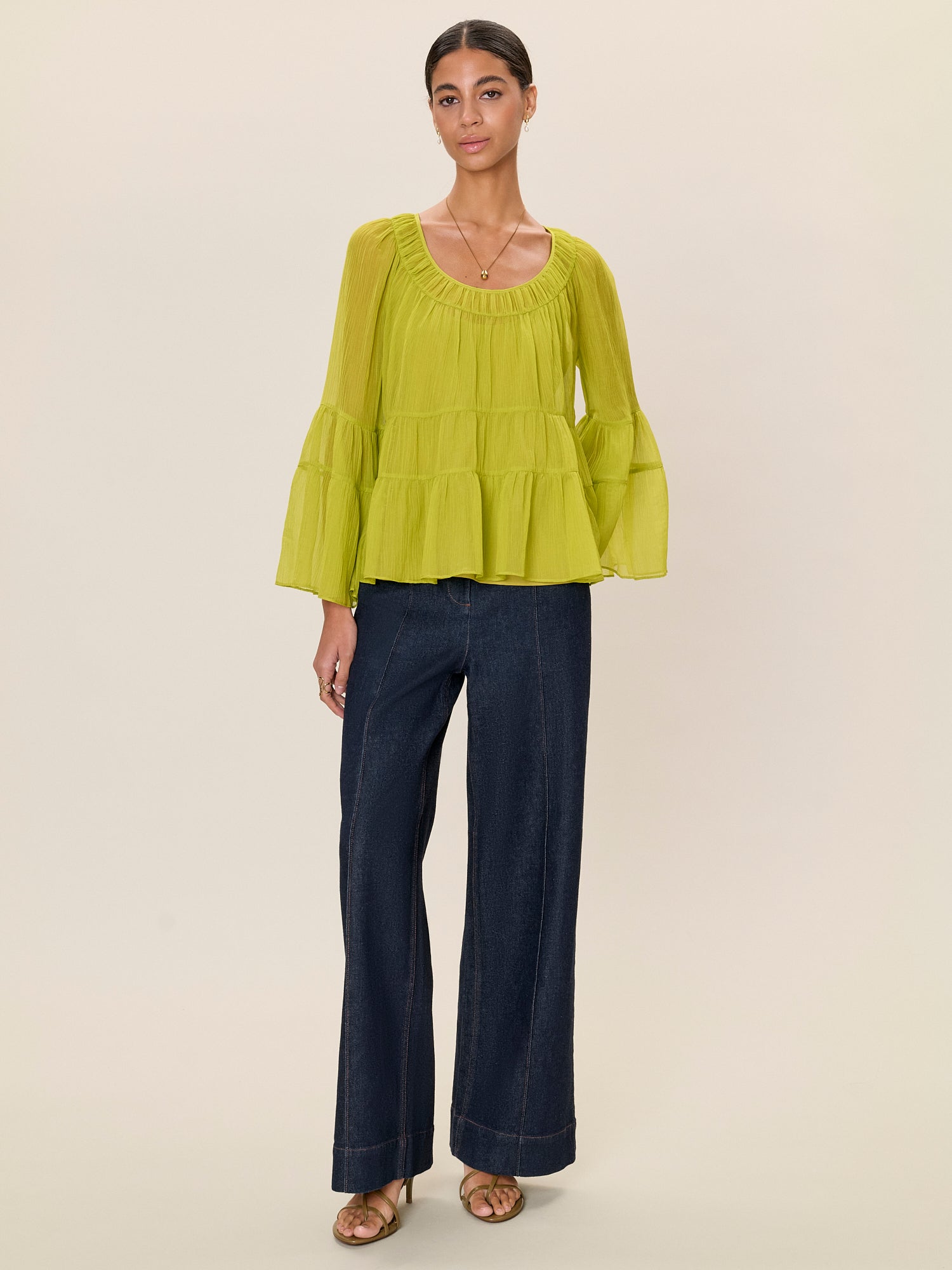 Woman wearing a green blouse and dark blue pants on a beige background