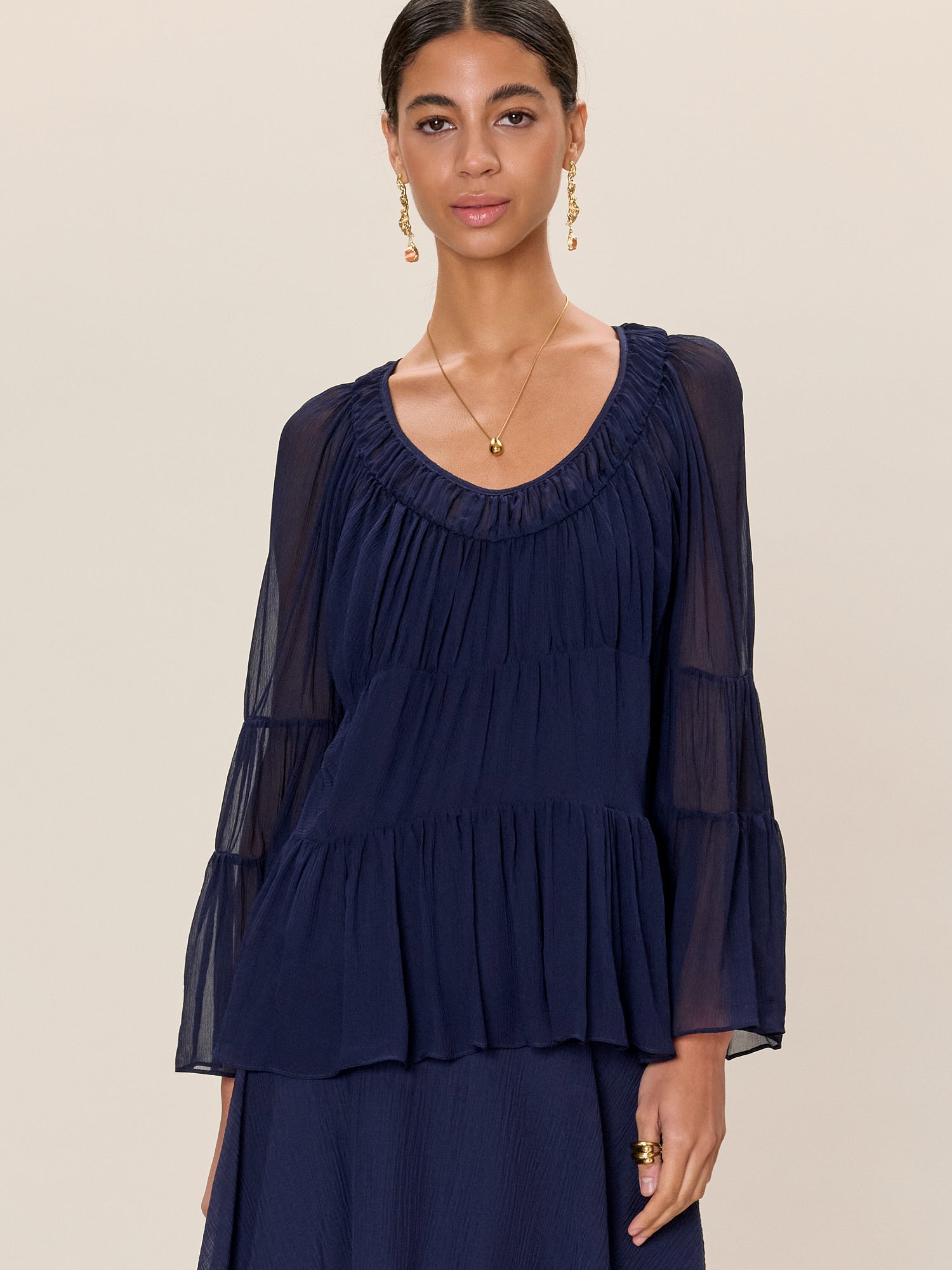 Woman wearing a navy blue dress with sheer sleeves against a beige background