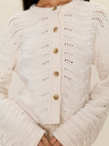 Close-up of a person wearing a white knitted cardigan with button details.