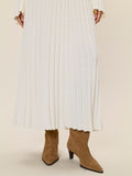 Person wearing a white pleated dress with brown suede boots on a plain background